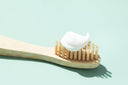 A bamboo toothbrush with toothpaste on a light aqua background