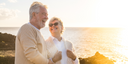 Oralieve image - Older man smiling looking to right with lady with sunglasses looking and smiling at man with the sea in background